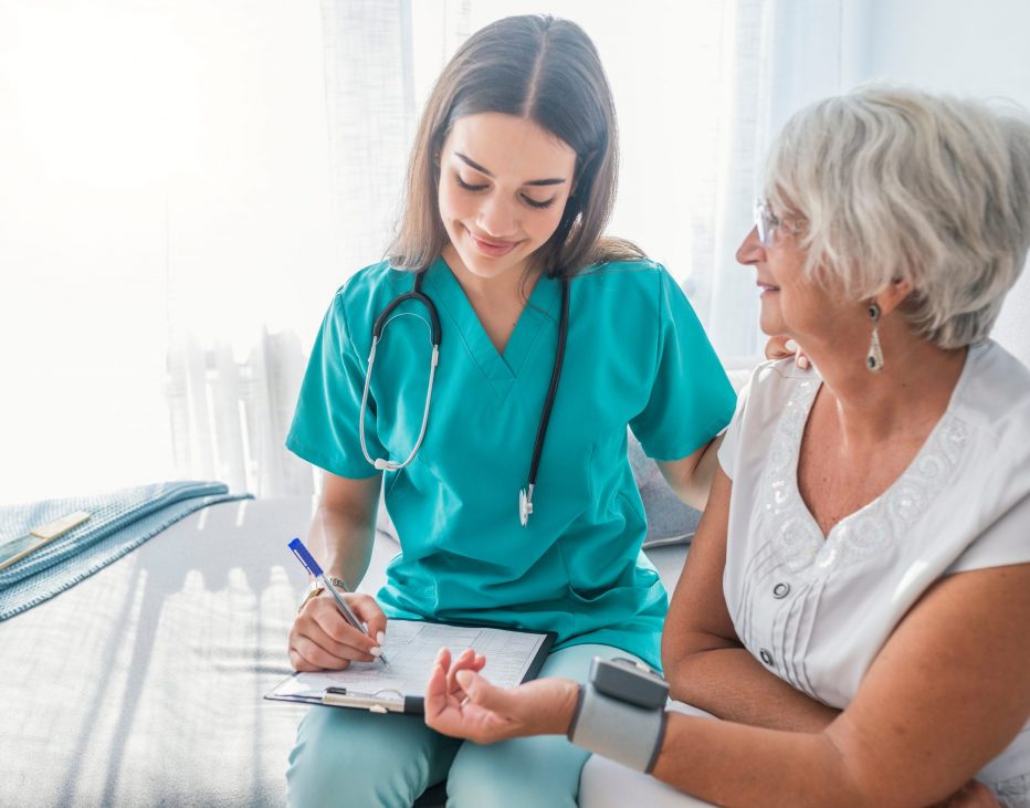 Nurse measuring blood pressure of senior woman at home. Smiling Nurse measuring blood pressure of senior woman at home. Smiling to each other. Young nurse measuring blood pressure of elderly woman at home. Doctor checking elderly woman's blood pressure